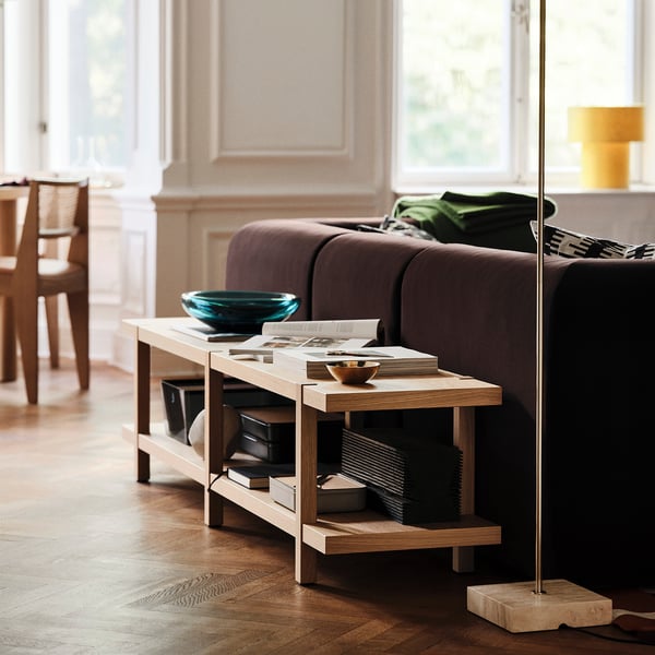 STOCKHOLM 2025 Bank aus hellem Holz, in der Nähe eines dunkelbraunen Sofas. Hält Zeitschriften, Schüssel und Bücher. Schlichtes, modernes Design.