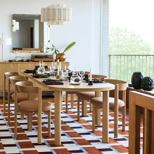 Modernes Esszimmer mit orange-blauem Teppich, Holztisch, Stühlen, Kronleuchter, Spiegel und Tageslicht.