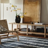 Ein Wohnzimmer mit einem Wollteppich mit Birkenmuster, einem Couchtisch, einem Stuhl und einer Vase mit gelben Blumen. Skandinavischer Minimalismus.