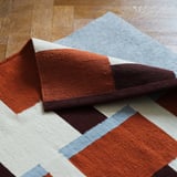 Ein handgewebter Wollteppich mit geometrischen Mustern, wendbar, der im Innenbereich auf einem Holzboden ausgestellt wird.