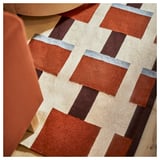 Handgewebter Teppich mit geometrischen Quadraten in Orange, Elfenbein und Braun auf hellem Holzboden.