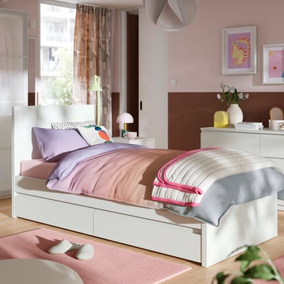 Weißes Bett mit lila/rosa Bettwäsche, hohem Kopfteil, 2 Aufbewahrungsboxen, rosa Zimmer.