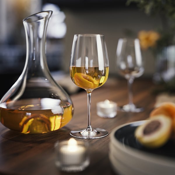 Tisch gedeckt mit durchsichtigen Gläsern, darunter eine Karaffe, Weingläser und ein leeres Glas. Konzipiert für Weißwein, zu Kerzen und Speisen.