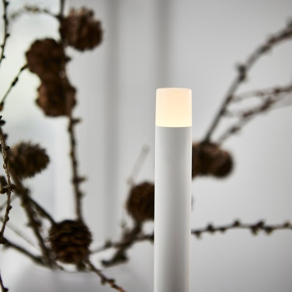 Moderne weiße LED-Kerze mit klarem Fokus, umgeben von weichen, unscharfen Ästen.