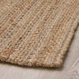Natürlicher Juteteppich aus nächster Nähe, gezeigt auf Holzboden. Dichte Weberei, strukturierte Oberfläche, robust und dennoch stilvoll.