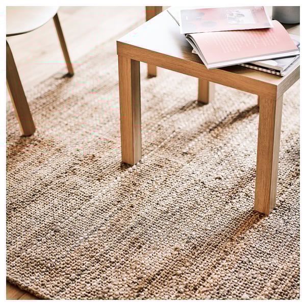 Ein Couchtisch auf einem strukturierten beigen Juteteppich mit einem Buch darauf, der natürliche Materialien und minimalistisches Design präsentiert.