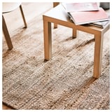 Ein Couchtisch auf einem strukturierten beigen Juteteppich mit einem Buch darauf, der natürliche Materialien und minimalistisches Design präsentiert.