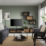 Modernes Wohnzimmer mit grünen Wänden, TV, grauem Sofa, gelben Kissen, Büchern und Tageslicht.