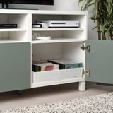 In einem weißen Schrank befinden sich Schallplatten, Spielekonsolen und Kopfhörer der STUK-Serie.