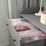 Offene graue Schublade mit weißen Trennwänden, rosa Kleidung und Accessoires im Inneren.