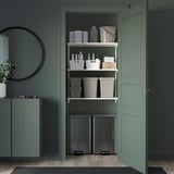 Ordentliches, organisiertes Regal aus weißem Metall mit Plastikbehältern, Flaschen und Reinigungswerkzeugen; Passt unter eine grüne Theke in einem Dekorationsraum.