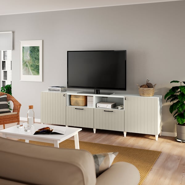 Modernes Wohnzimmer mit hellgrau gestrichenem TV-Ständer, großem Flachbildfernseher, weißem Couchtisch, beigem Sofa und natürlichen Pflanzen.