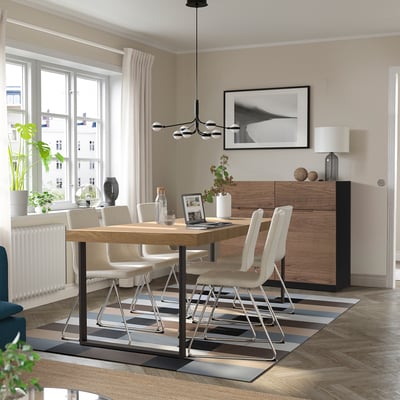 Ausziehbarer Esstisch aus Eiche für 6-8 Personen, mit Metallgestell und gestreiftem Teppich. Leichte Stühle, großes Fenster und Pendelleuchte im minimalistischen Raum.