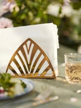 Goldener Serviettenhalter, TILLSTÄLLNING, Fächerform, auf Tisch mit Glas, begrünt.