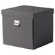 Eine graue TJOG-Aufbewahrungsbox mit Deckel und einem Etikettenhalter aus Metall auf der Vorderseite. Es ist rechteckig und für die Organisation verschiedener Gegenstände konzipiert.