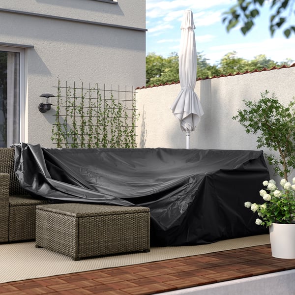 Hinterhofterrasse mit TOSTERÖ-Abdeckung. Es schützt Möbel vor Regen, Sonne, Schmutz und Staub. Schwarzer Bezug auf Korbcouch in der Nähe von Wand und Pflanzen.