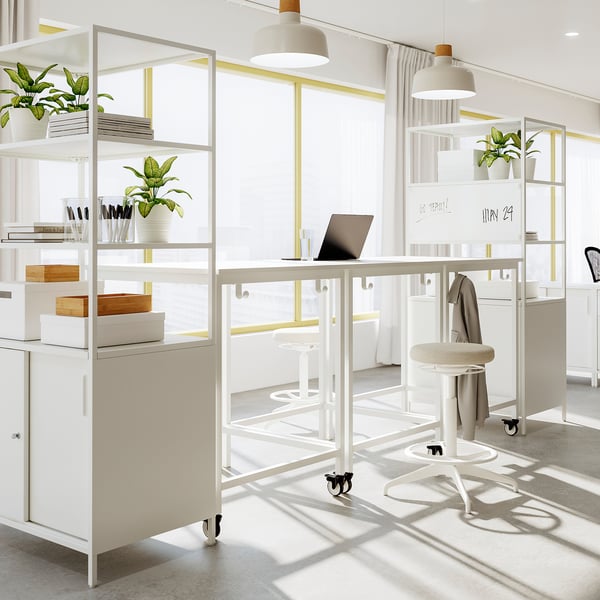 Moderne weiße Büroeinrichtung mit TROTTEN-Besprechungstischen, Regalen mit Pflanzen und einem Laptop. Helles und minimalistisches Design.