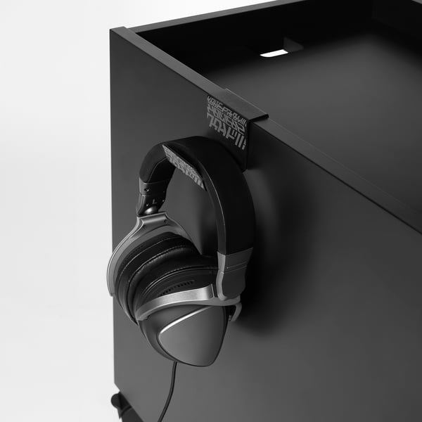 Schwarzer Gaming-Schubladenschrank mit Headset-Haken. Der Kopfhörer hängt an einem seitlichen Haken und ist einsatzbereit.