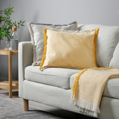 Hellgraues Sofa mit großen Kissen mit gelben Fransen.