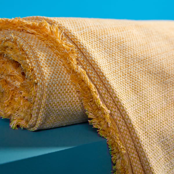 Gelber gewebter Überwurf mit Fransen auf blauem Hintergrund.