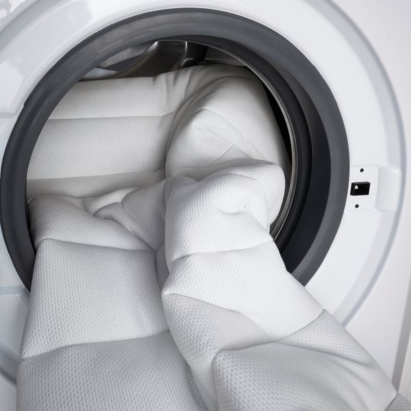 Weiße Waschmaschine mit großem weißem Handtuch im Inneren, das ihre geräumige Trommel demonstriert.