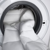 Weiße Waschmaschine mit großem weißem Handtuch im Inneren, das ihre geräumige Trommel demonstriert.