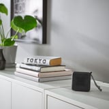 Der kleine schwarze VAPPEBY-Lautsprecher steht neben Büchern auf einem weißen Regal.