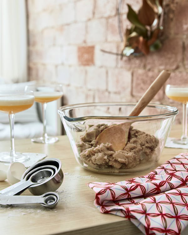 Holzlöffel in einer Glasschüssel mit Teig auf dem Tisch mit Messbechern und Weingläsern.