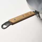 Nahaufnahme eines robusten Wok-Griffs mit Holzgriff und Metallschlaufe, der mit Schrauben sicher befestigt ist und ein robustes Design auf einem sauberen weißen Hintergrund zeigt.