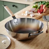 Flacher Wok mit Holzgriff auf der Küchentheke, bereit zum Kochen. Frisches Gemüse in der Nähe, was zum Braten in der Pfanne einlädt.