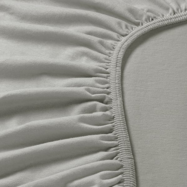 Nahaufnahme eines weichen, weißen Baumwolljersey-Bettlakens mit elastischem Rand, das eine glatte Textur und robuste Nähte aufweist.