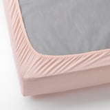 Ein Bettspannbetttuch mit hellrosa Jersey-Stoff und elastischen Kanten, das die Matratze auch in Ecken perfekt abdeckt.