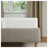 Modernes Bett mit weißem gestepptem Kopfteil und grauem Polstergestell, ordentlich an einem Fenster mit Vorhängen positioniert.
