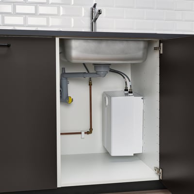 Die Ansicht unter dem Spültisch zeigt einen drucklosen Warmwasserbereiter, der über Kupferrohre mit einer verchromten VENSJÖN-Mischbatterie verbunden ist und einen reibungslosen Wasserfluss gewährleistet.