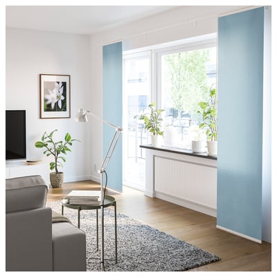 Helles, modernes Wohnzimmer mit großen Fenstern, grauer Couch, Pflanzen und einer Lampe.