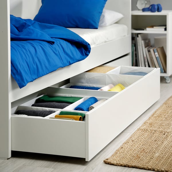 Schubladen unter dem Bett mit farbcodierter, gefalteter Kleidung, die den Platz maximiert.