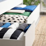 Weiße Schubladenschränke unter einem Bett organisieren gefaltete Decken in verschiedenen Farben und Mustern ordentlich und optimieren so den Stauraum effizient.