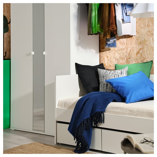 Modernes Schlafzimmer mit weißem VIHALS-Tagesbett, blauer Decke, bunten Kissen, grauen Schubladen und Kleiderständer.