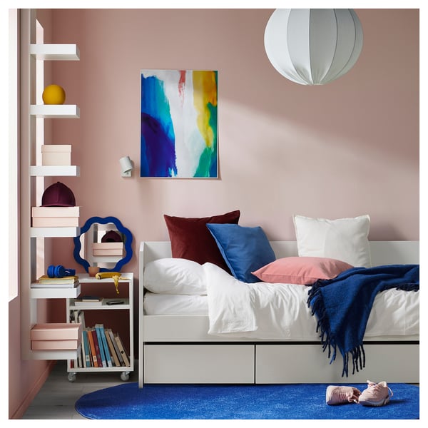 Modernes Schlafzimmer mit weißem Tagesbett, blau-weißem Dekor, farbenfroher Kunst und einem mobilen Regal.
