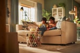 Kinder spielen auf dem VIMLE-Sofa mit Snacks und Pflanzen in einem sonnigen Raum.