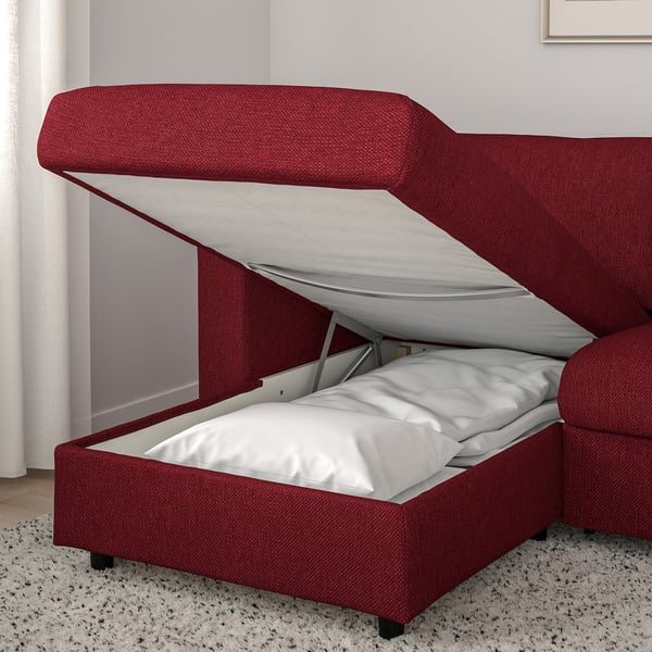 Rotes Schlafsofa mit Stauraum, offener Deckel mit Matratze und Bettwäsche, graue Vorhänge.