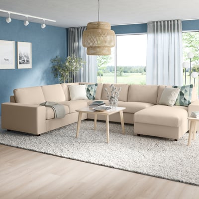 Minimalistisches Wohnzimmer: beiges Ecksofa, beiger Teppich, hellblaue Wände, natürliche Pendelleuchte. Große Fenster bieten Gartenblick.