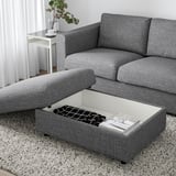 Modernes Wohnzimmer mit einem grauen VIMLE-Sofa und einer Ottomane. Die Ottomane verfügt über einen anhebbaren Sitz, der Stauraum mit Büchern und einer Fernbedienung im Inneren freigibt.