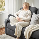 Frau entspannt sich auf grauem VINLIDEN-Sofa, hält einen Becher in der Hand und vertieft in ein Buch. Gemütliches Wohnzimmer.