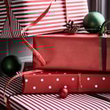 Gestapelte verpackte Geschenke mit roten Bändern und Ornamenten, die festliche Geschenkpapierdesigns und hochwertige Verpackungen präsentieren.