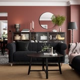 Gemütliches Wohnzimmer mit rostroten Wänden, schwarzem Sofa und deren Dekor, einschließlich Pflanzen und stilvoller Tischlampe.