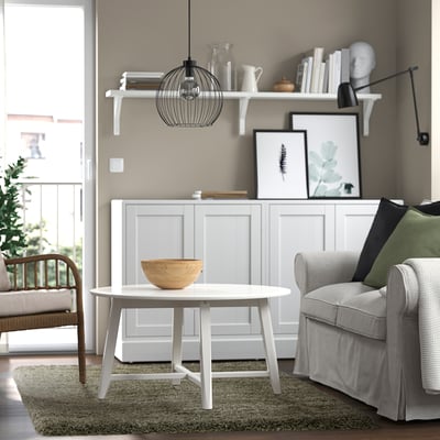 Gemütliches Wohnzimmer: Couchtisch, Schüssel, Sessel, Kissen, Teppich, Wände, Tür, Korbstuhl, Bücherregal.