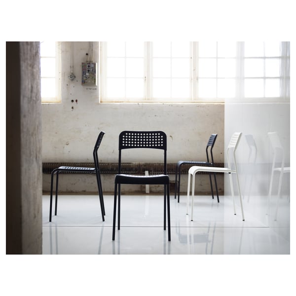 Room with three modern, stackable chairs - two black, one white - against concrete wall.