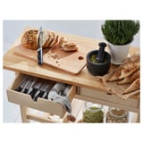 Wooden kitchen cart with open drawer showing knives, loaf of bread, mortar with pestle, plant, and jars with spices.