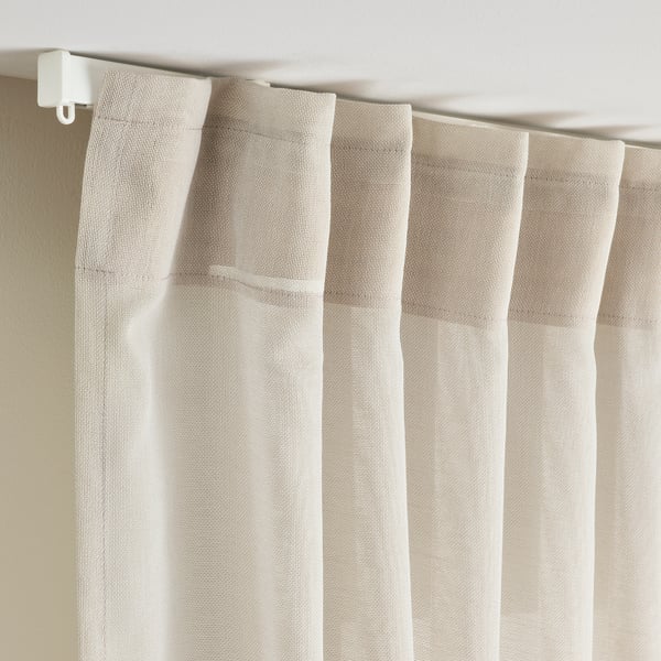Light beige sheer curtain with visible folds and a white curtain rod. Allows light and shapes to filter through, ideal for wider windows.